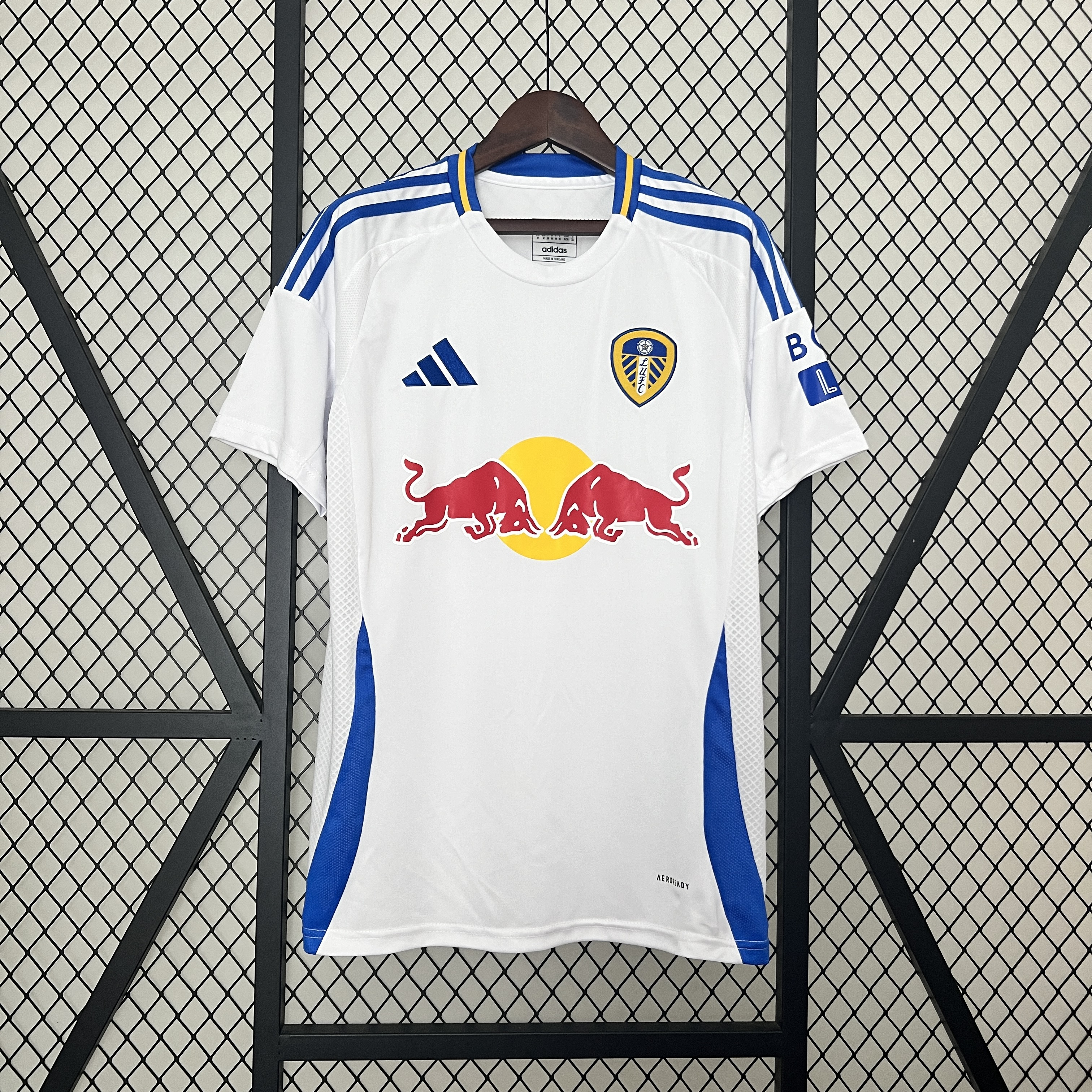 Mens Leeds United Home Jersey 2024/25 Mens Leeds United Home Jersey 2024/25 on hanger showing white body with royal blue shoulder stripes and Red Bull sponsor