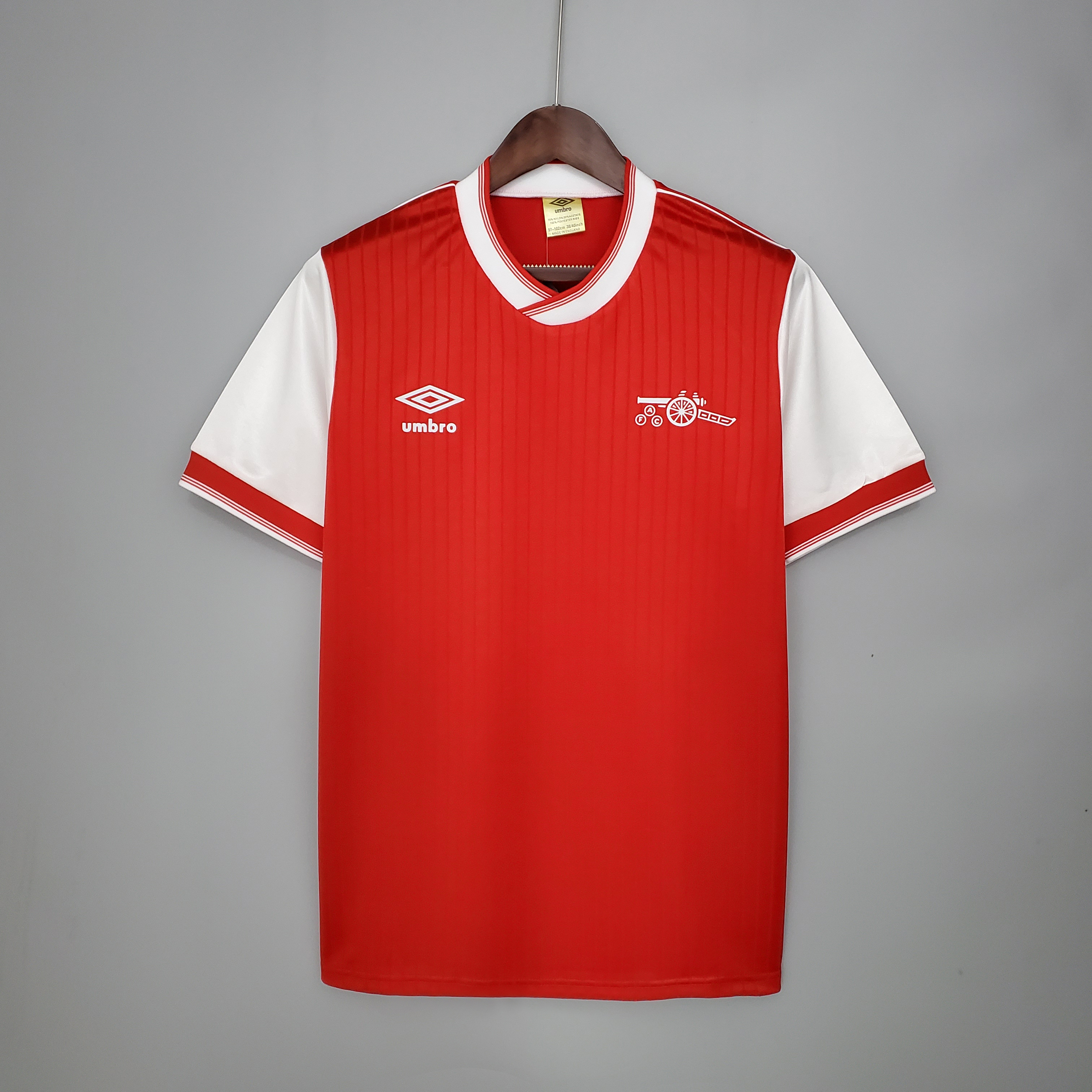 Mens Arsenal Retro Home Jersey 1983/86 Mens Arsenal Retro Home Jersey 1983/86 on hanger showing red pinstriped body with white raglan sleeves and cannon badge