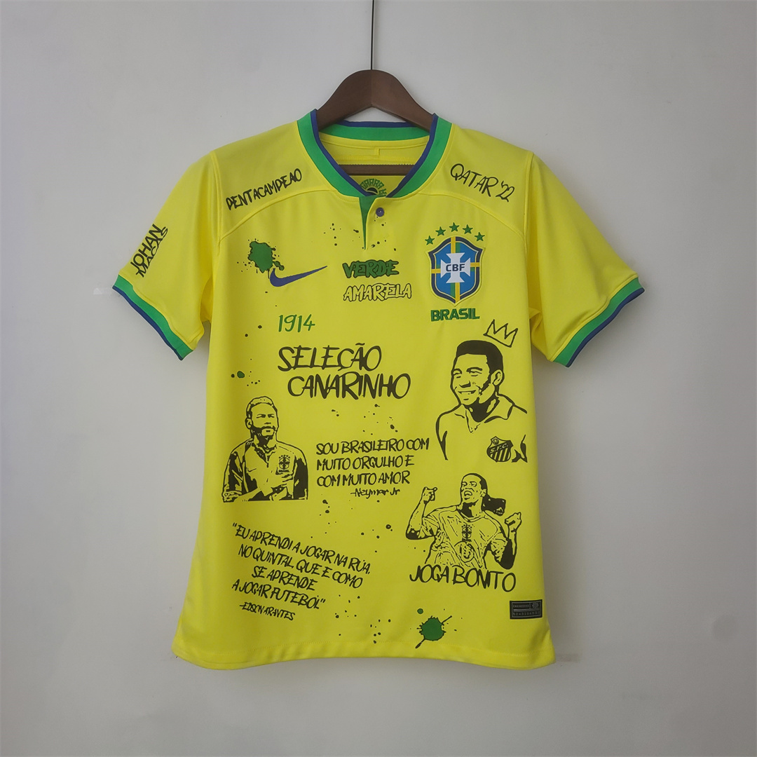 Mens World Cup Brazil Court Graffiti Board Home Jersey 2022 Mens World Cup Brazil Court Graffiti Board Home Jersey 2022 on hanger showing yellow jersey with graffiti portraits