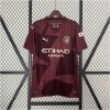 Mens Manchester City Third Jersey 2024/25 on hanger showing maroon body with tonal geometric panels and gold sponsor