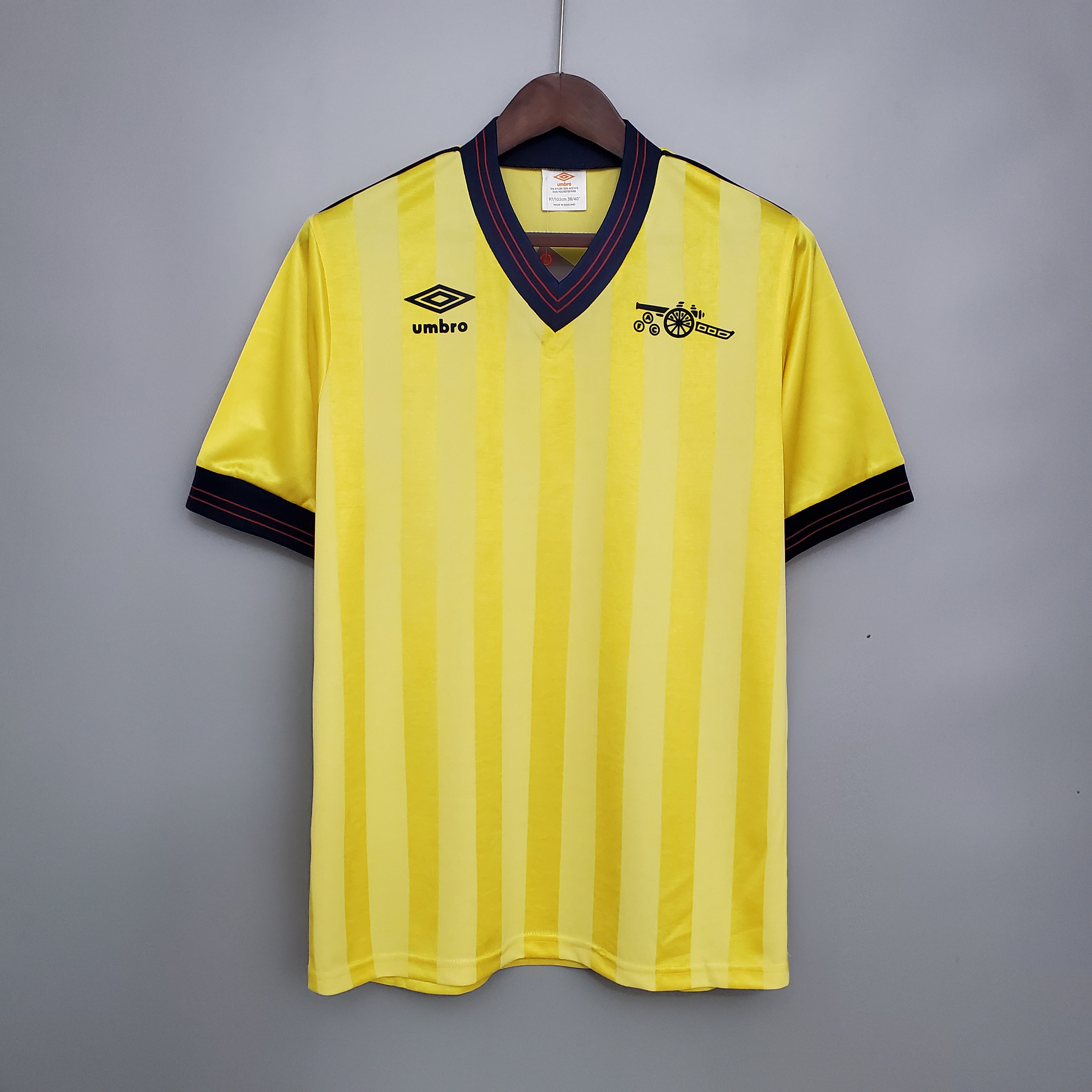 Mens Arsenal Retro Away Jersey 1983/86 Mens Arsenal Retro Away Jersey 1983/86 on hanger showing canary yellow shadow-stripe body with navy V-neck and cannon badge