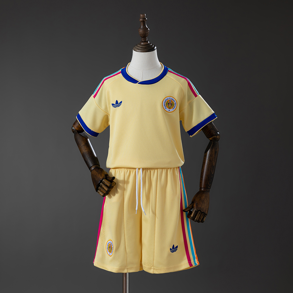 Kids Curacao Away Kit 2026 Front view of the Kids Curacao Away Kit 2026 showcasing pastel yellow fabric, colorful shoulder stripes, and matching yellow shorts on a mannequin.