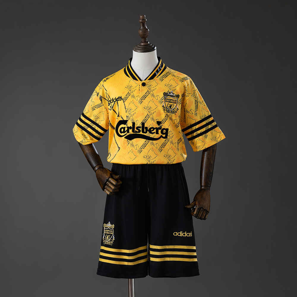 Kids Liverpool Retro Third Kit 1994/96 Kids Liverpool Retro Third Kit 1994/96 front view featuring yellow jersey and black shorts with Carlsberg sponsor