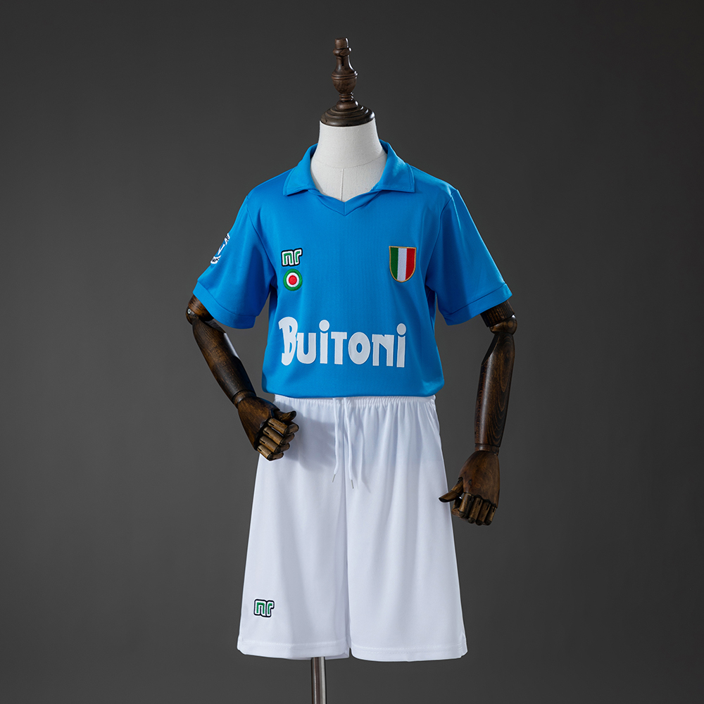 Kids Napoli Retro Home Kit 1987/88 Kids Napoli Retro Home Kit 1987/88 front view in sky blue with Scudetto shield, Buitoni sponsor, and white shorts