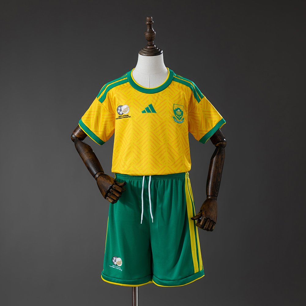 Kids South Africa Home Kit 2026 Kids South Africa Home Kit 2026 front view featuring yellow jersey with green trim and green shorts