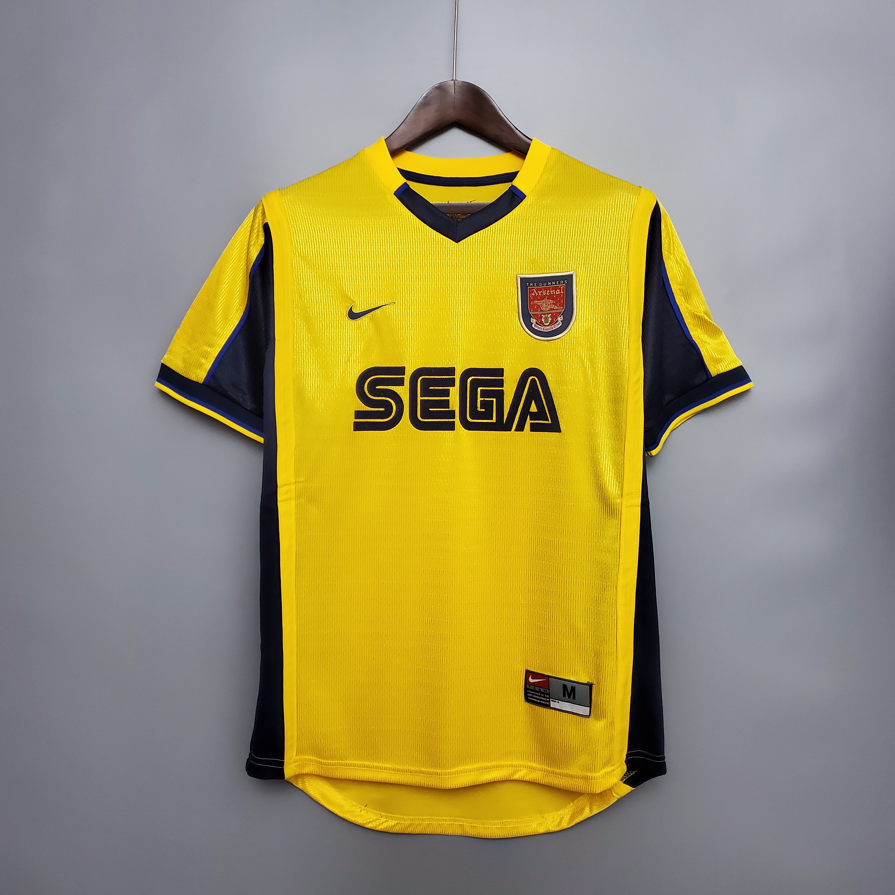 Mens Arsenal Retro Away Jersey 1999/00 Mens Arsenal Retro Away Jersey 1999/00 on hanger showing vibrant yellow body with navy side panels, cannon crest, and SEGA logo