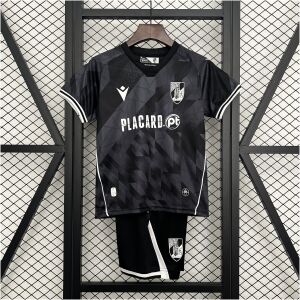 Kids Vitoria SC Away Kit 2025/26 on rack showing charcoal black geometric jersey with white trims and matching shorts